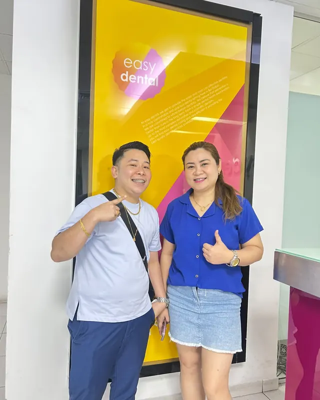 Two smiling patients with braces in front of the Easy Dental sign