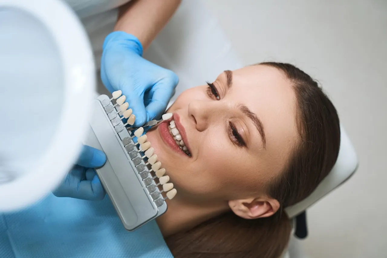 Dentist holding a tooth shade guide next to a patient's smile